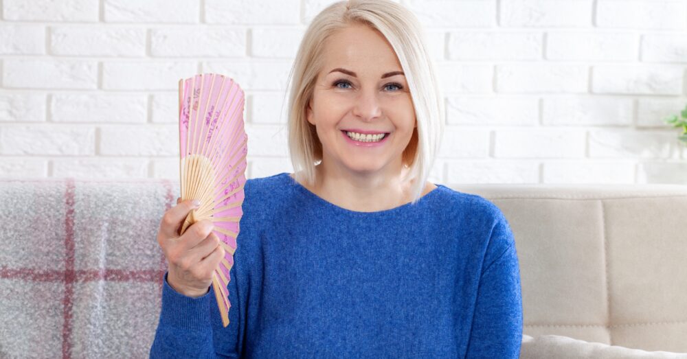 A smiling woman in a blue sweater holding a fan