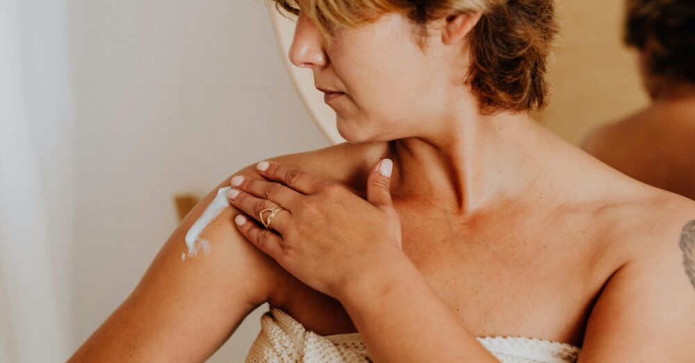 Woman applying a hormone replacement therapy cream to her shoulder at home