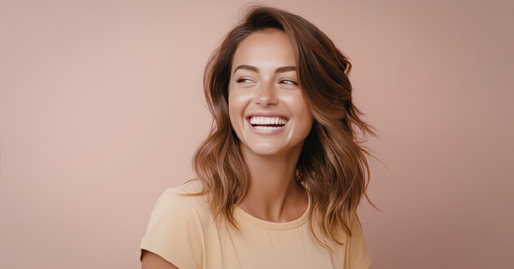 Woman with wavy brown hair laughing and looking relaxed against a warm neutral background