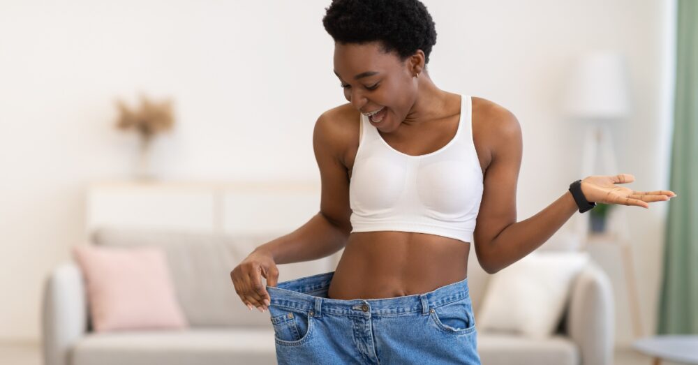 Woman holding out her oversized jeans showing significant weight loss results