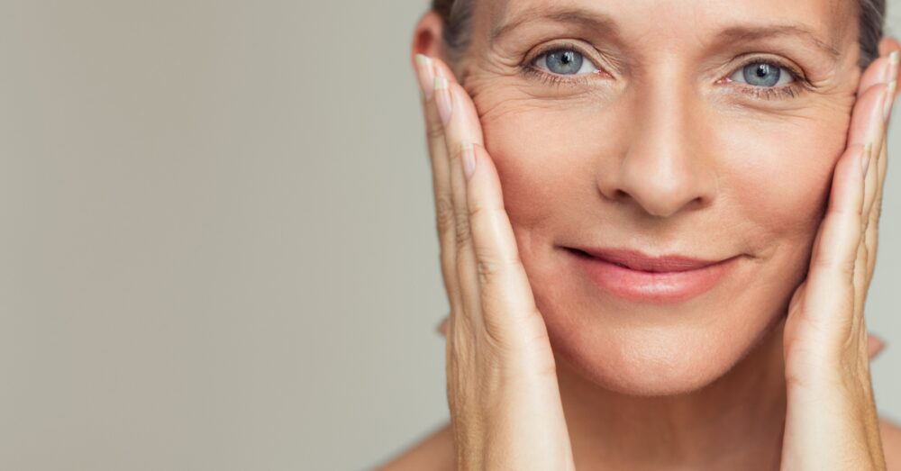 A middle-aged woman touching the sides of her face while smiling