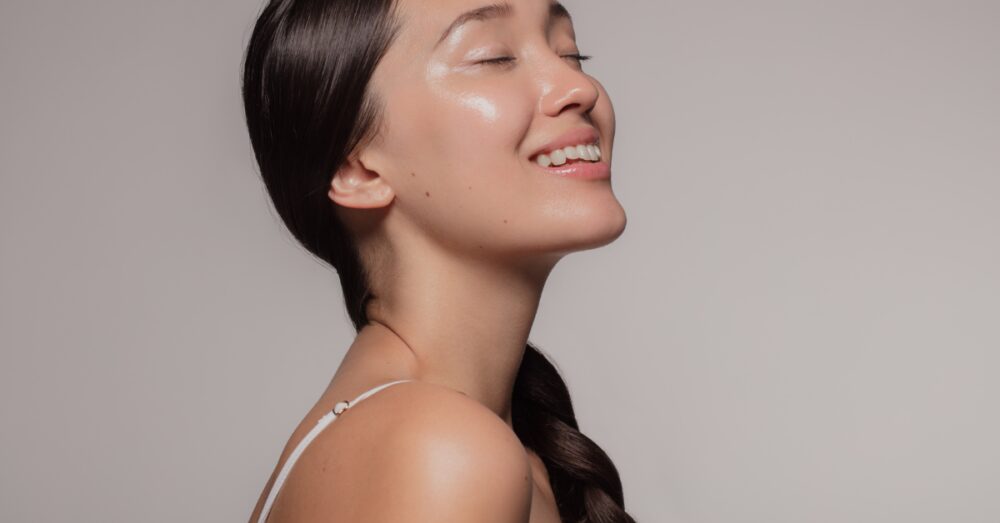 A woman with glowing skin smiling with her eyes closed